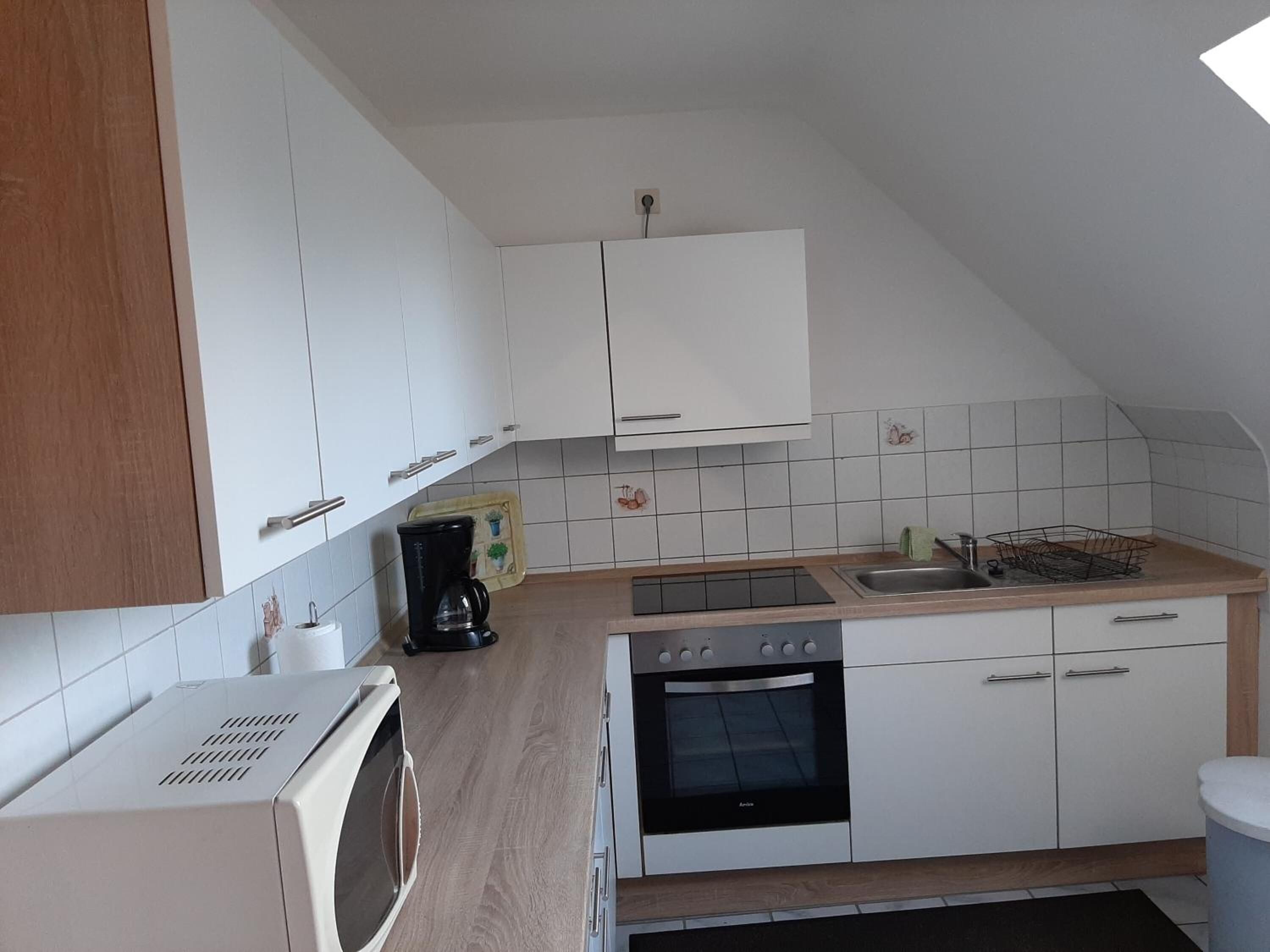 A compact kitchen with white cabinets, a built-in oven, a microwave, and a coffee maker.