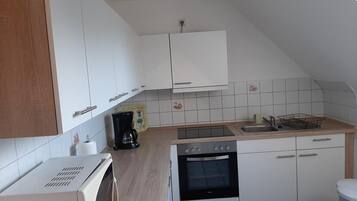 A compact kitchen with white cabinets, a built-in oven, a microwave, and a coffee maker.