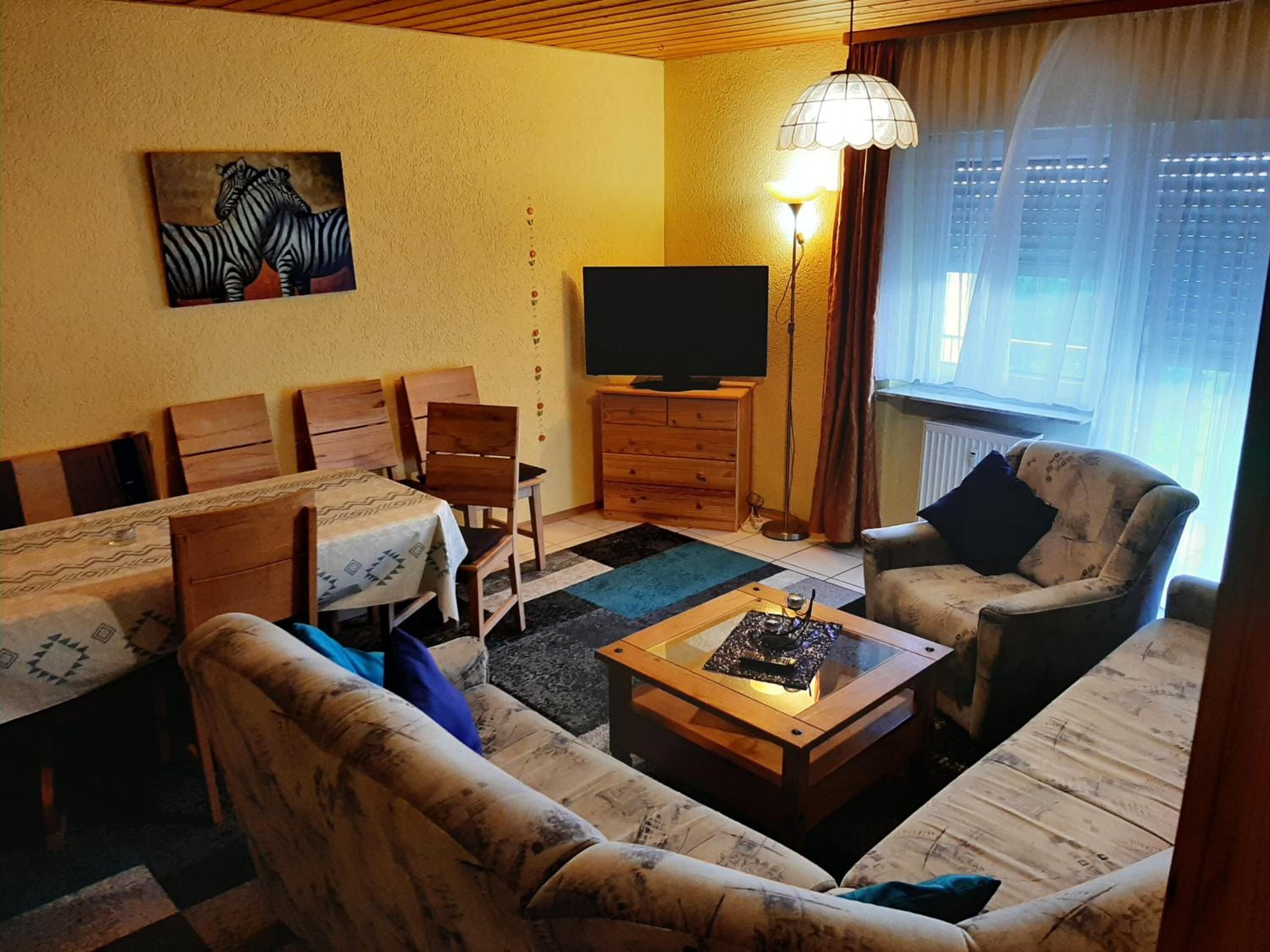A cozy living room with a sofa, a coffee table, a TV, and a dining table with chairs.