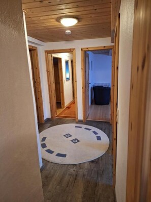 Kapea käytävä, jossa on puulattia ja pyöreä, geometrisin kuvioin koristeltu matto.