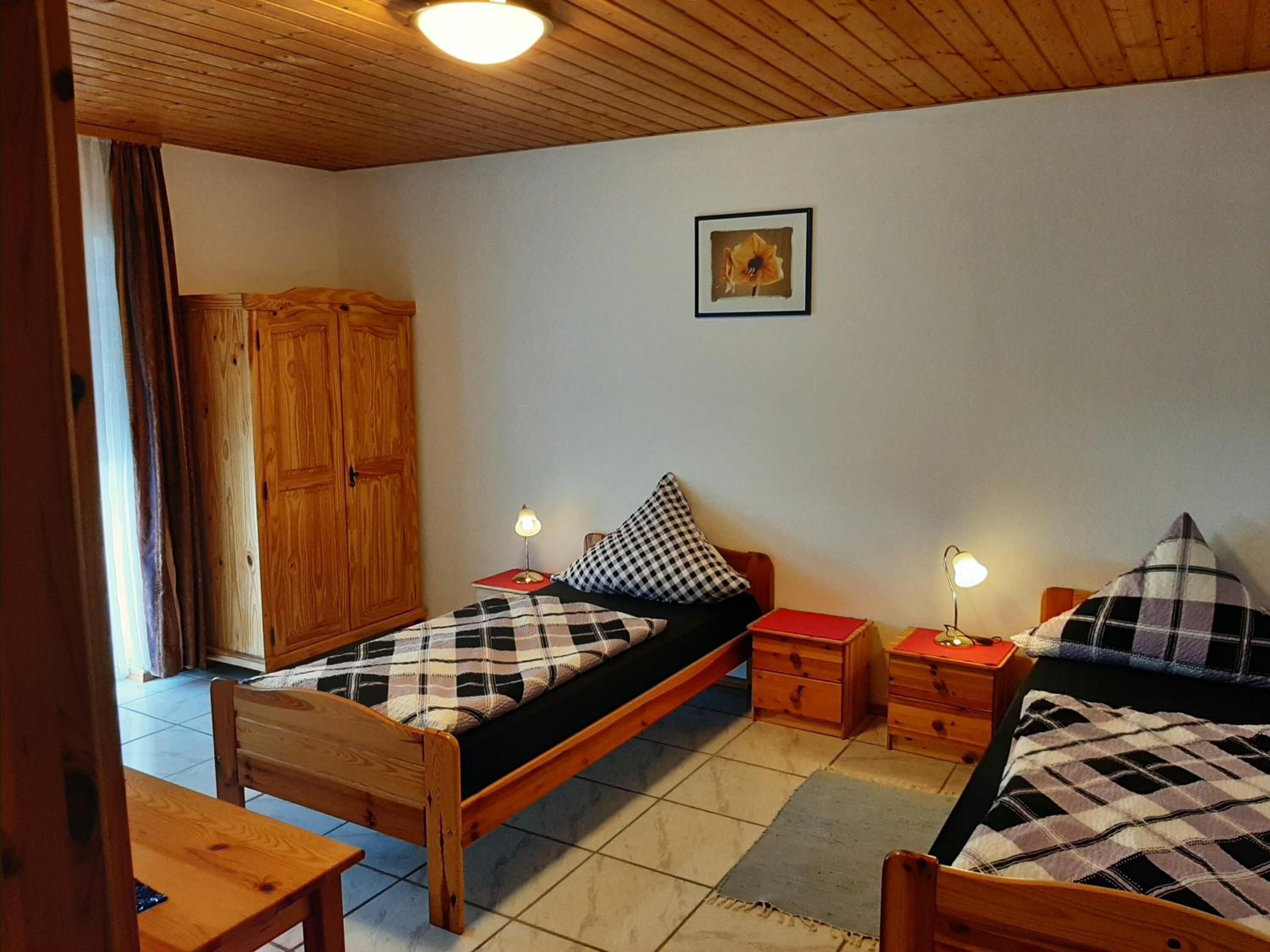 Ein gemütliches Schlafzimmer mit zwei Einzelbetten, Holzmöbeln, einem Kleiderschrank und einem gerahmten Bild an der Wand.