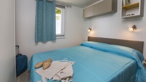 Un dormitorio con una cama, una maleta y un ventanal con cortina.