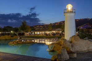 A white lighthouse, a swimming pool, and a building with outdoor seating. - Càmping Valldaro (Castell-Platja d'Aro)