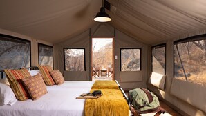 Une pièce aménagée avec une tente, un lit, des oreillers, une table, des chaises et une vue sur les arbres.