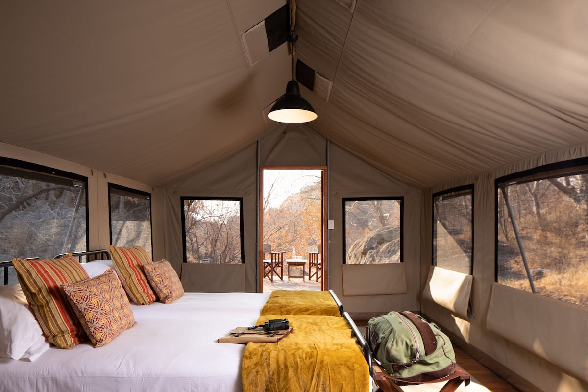 Una habitación con carpa, una cama, almohadas, una mesa, sillas y vistas a árboles.
