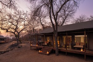 A rustic cabin with a covered porch, wooden deck, and outdoor seating area.