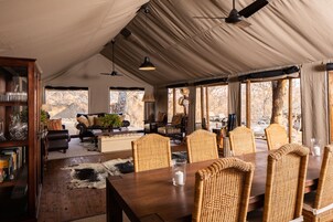 A tented room with a dining table, wicker chairs, and a leather sofa.