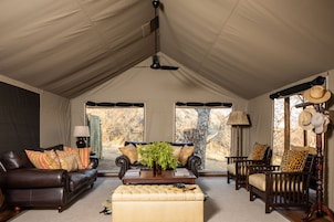 A tented room with a sofa, armchairs, a coffee table with a plant, and a lamp.