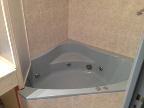 Una bañera en esquina con ducha integrada, paredes de azulejos y una encimera blanca.