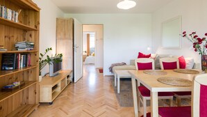 Ein modernes Wohnzimmer mit einer Holzbücherreolen, einem Fernseher, einem Esstisch mit roten Stühlen und einem großen Spiegel an der Wand.