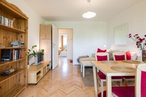 A modern living room with a wooden bookshelf, a TV, a dining table with red chairs, and a large mirror on the wall. - KrakowRentals - Kazimierz Apartment (Kraków)