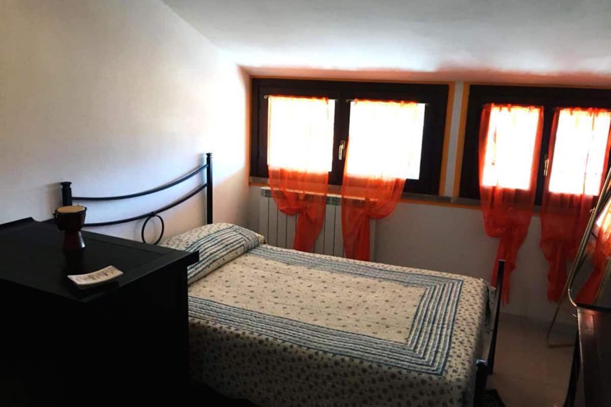 Una habitación pequeña con cama individual, ventana y mesita de noche.