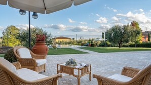 Terrassa exterior amb mobles de vimet, una taula amb objectes decoratius i una vista a una piscina i una casa al fons.