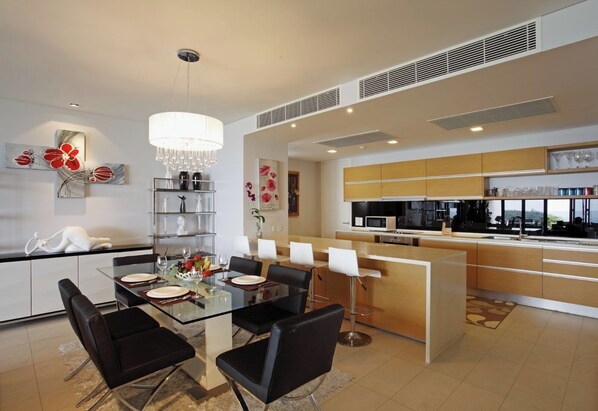 A modern kitchen with a central island, a dining area with a glass table, and a view through the window. - The heights B18 Seaview near Kata Beach (Karon)