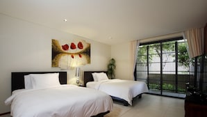 A hotel room with two beds, a painting on the wall, a potted plant, and a view of greenery through the window. - The heights B18 Seaview near Kata Beach (Karon)