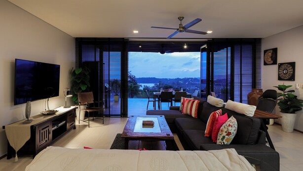 A modern living room with a flat-screen TV, a ceiling fan, and a large window offering a view of the outdoors. -  The Heights Kata Seaview C1 near Kata Beach (Karon)