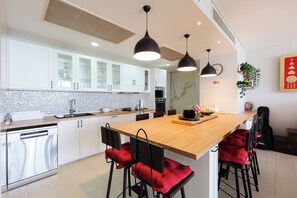 Uma cozinha moderna com armários brancos, uma ilha de madeira e banquetas com almofadas vermelhas.