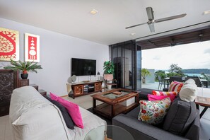 A modern living room with a sofa, coffee table, and a television. There is a balcony with a view of the ocean.
