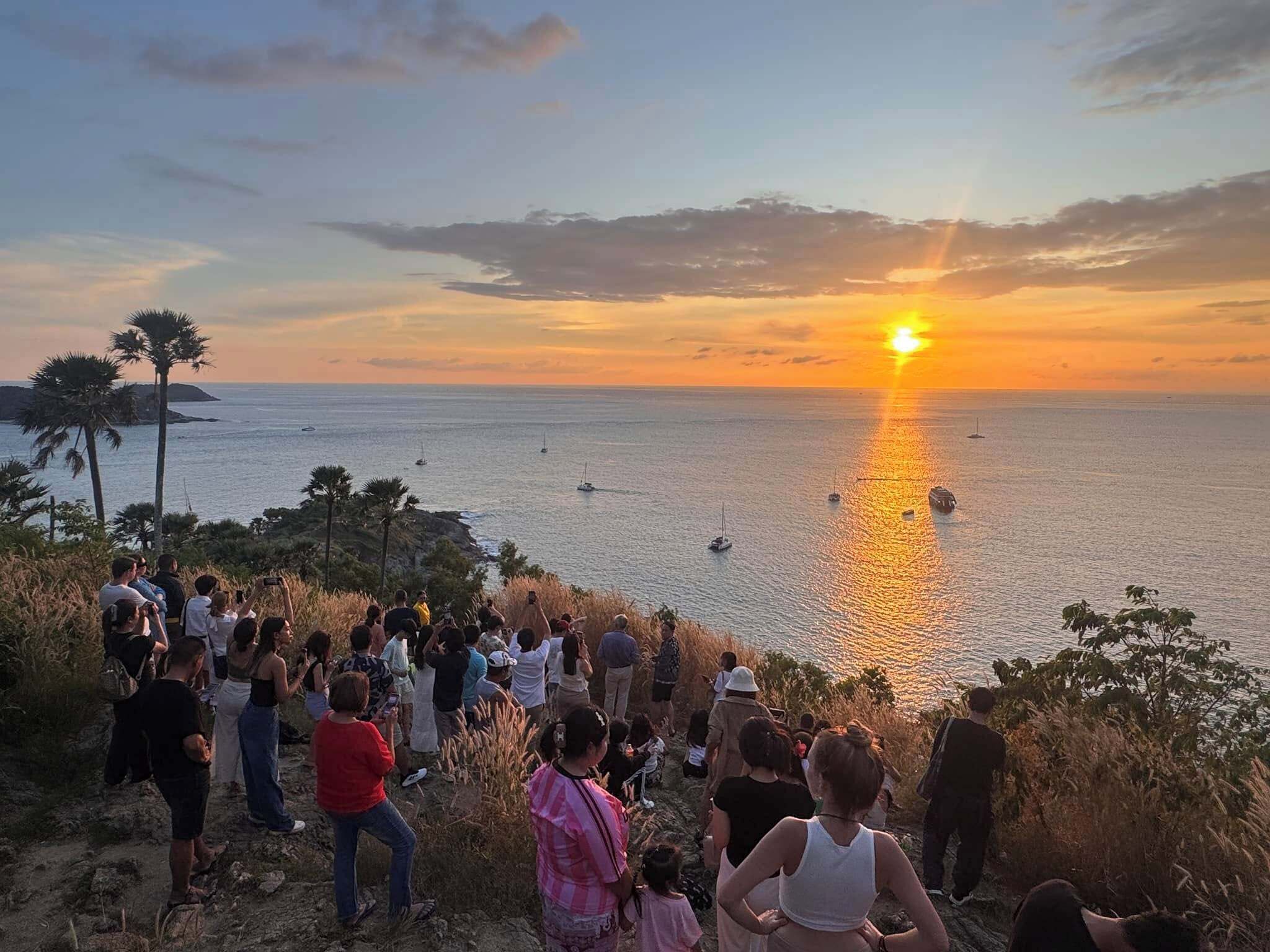Vista del atardecer sobre una zona costera, con gente reunida en una colina.