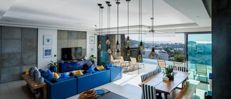 Ein modernes Wohnzimmer mit einem blauen Sofa, einem Esstisch und Blick auf die Stadt.