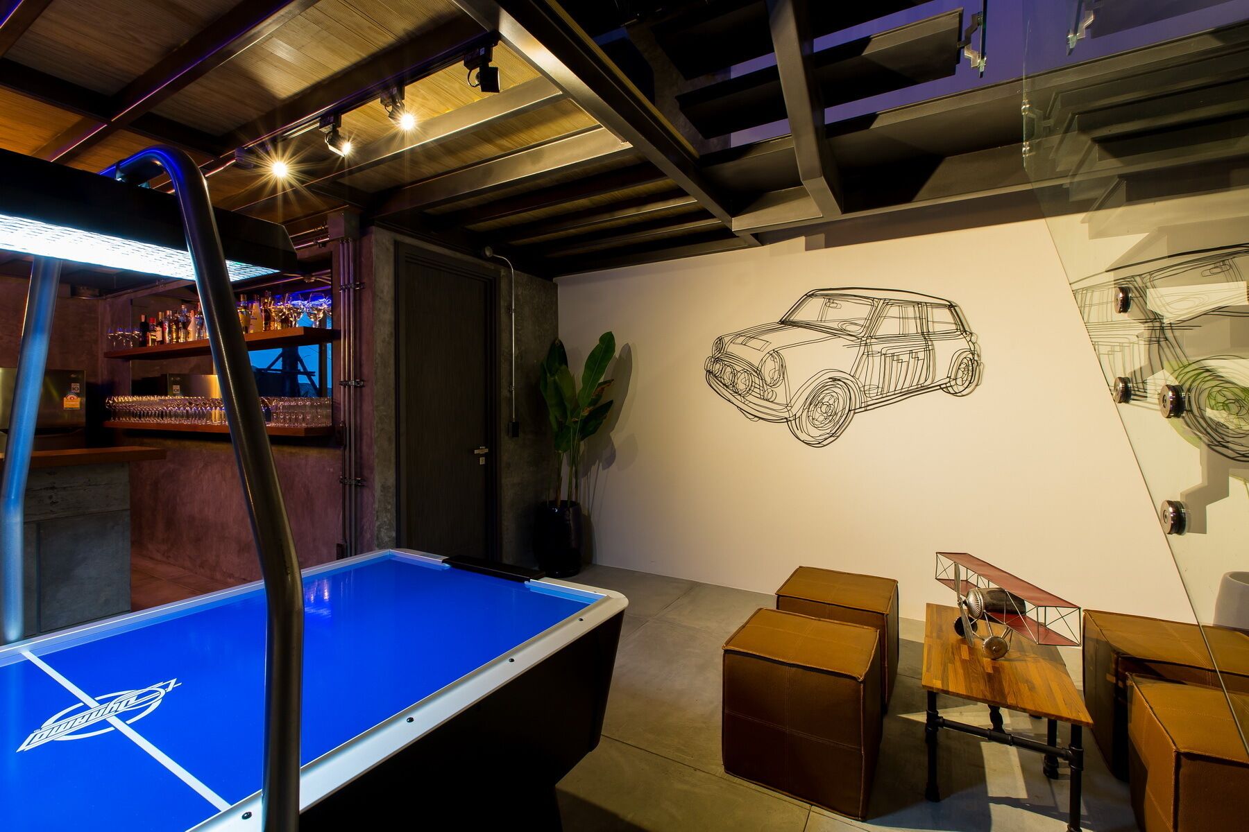 A billiards table with a logo, a bar area with bottles, a wall with a car sketch, and a model airplane.