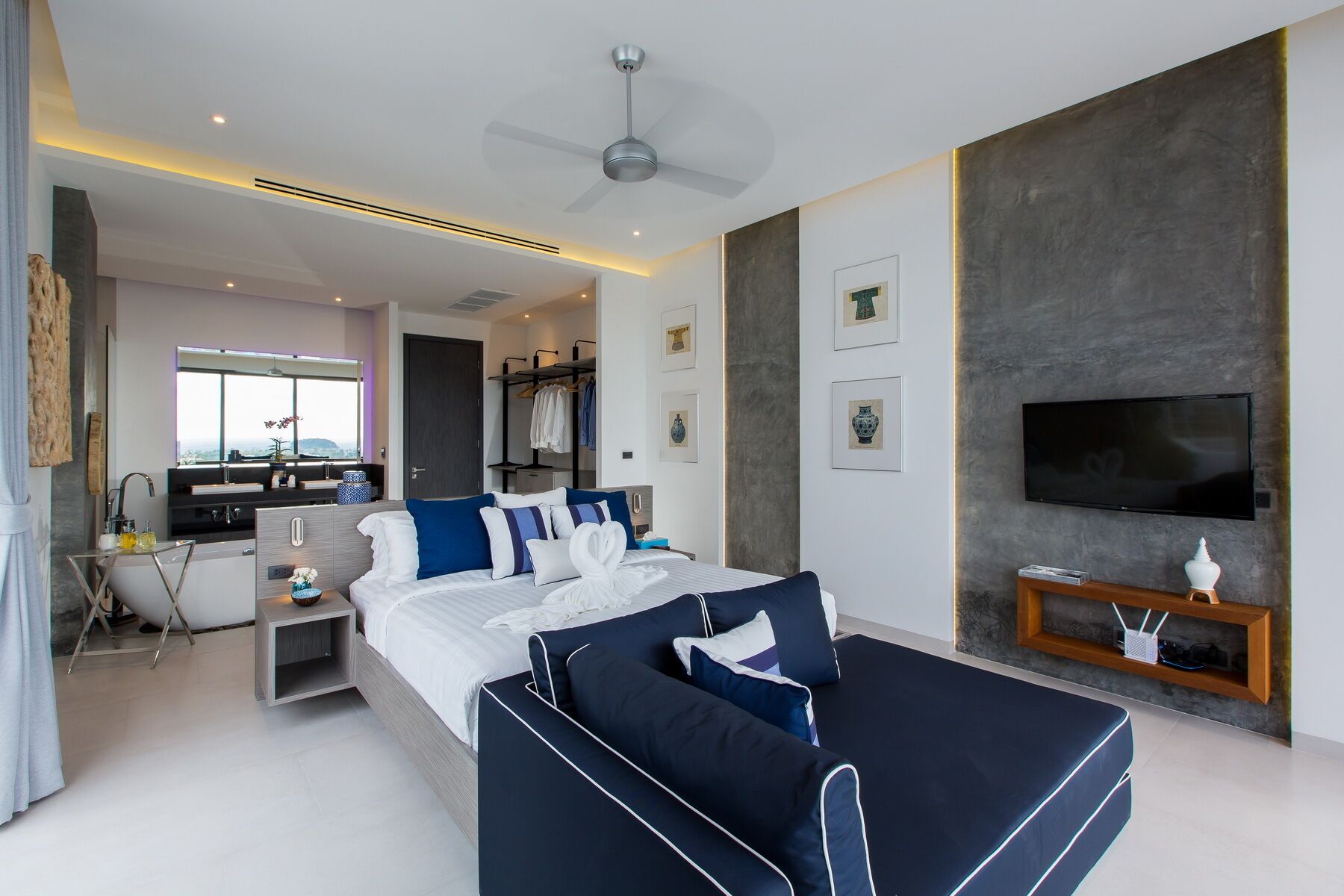 A modern hotel room with a bed, a TV, a desk, and a seating area.