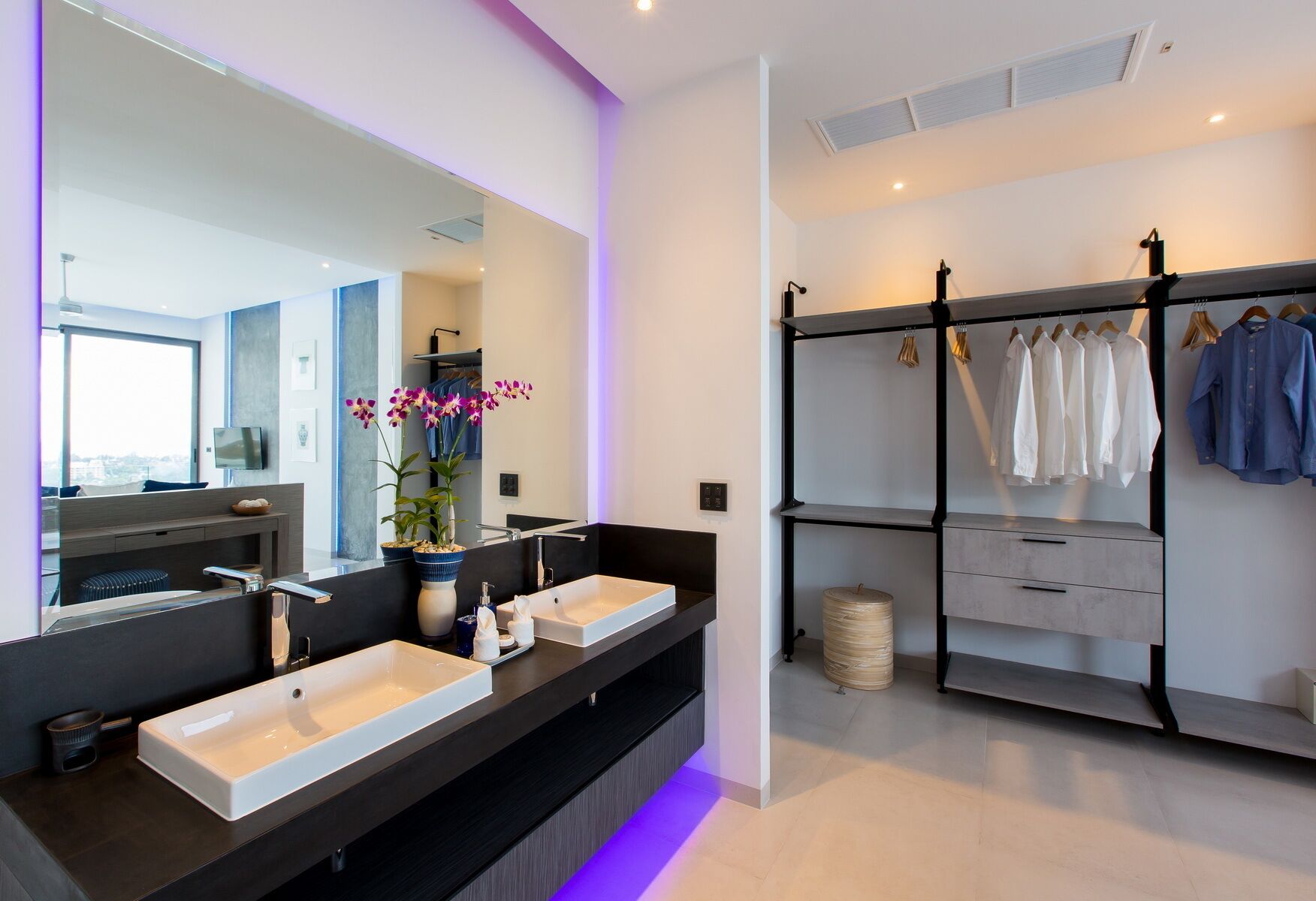 Une salle de bain moderne avec deux vasques, un grand miroir et un porte-vêtements.