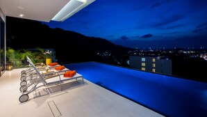 A rooftop pool area with a seating arrangement and a view of the city at dusk. - Villa Omari Luxury Seaview Pool & Game Room (Karon)