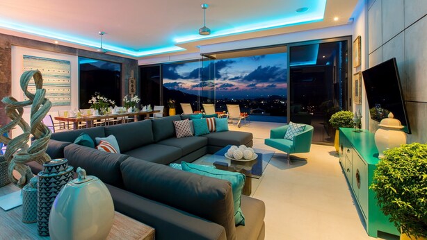 A modern living room with a sectional sofa, a dining area, and a large TV. - Villa Omari Luxury Seaview Pool & Game Room (Karon)