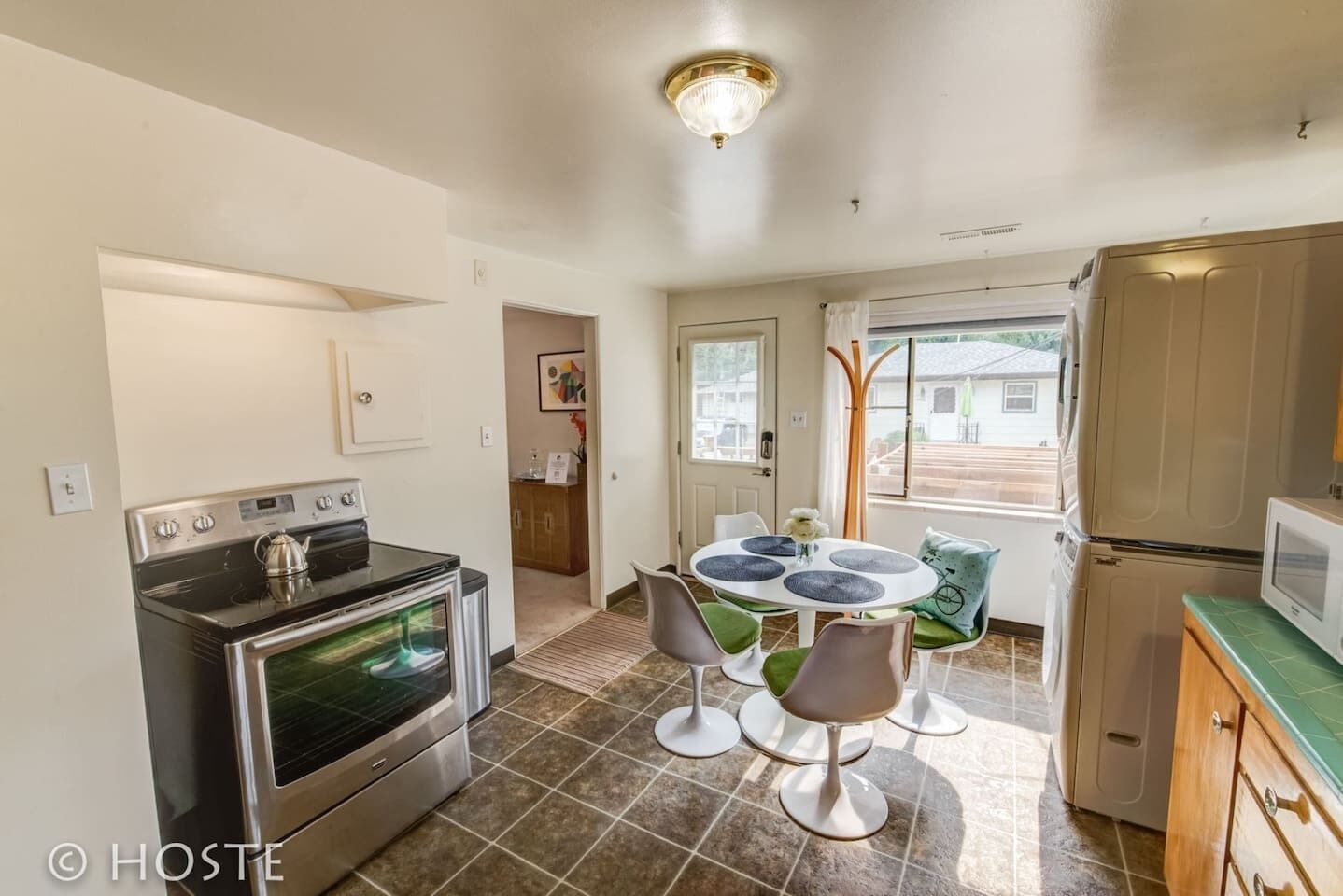 A compact kitchen with a stove, oven, and refrigerator. There is a dining table with chairs and a window with a view of the outside.