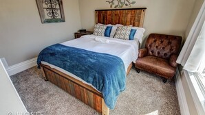 A bedroom with a wooden bed, a blue blanket, a brown leather chair, and a decorative wall piece. - 3 BR Beautifully Restored 1890`s Homedowntown (Colorado Springs)