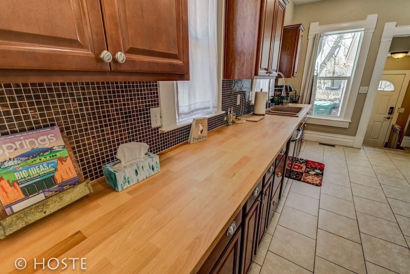 A kitchen with wooden cabinets, a tiled backsplash, a wooden countertop, and a window with a view of the outside.