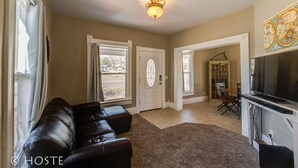 A spacious living room with a leather sofa, a television, and a dining area with a table and chairs. - 3 BR Beautifully Restored 1890`s Homedowntown (Colorado Springs)
