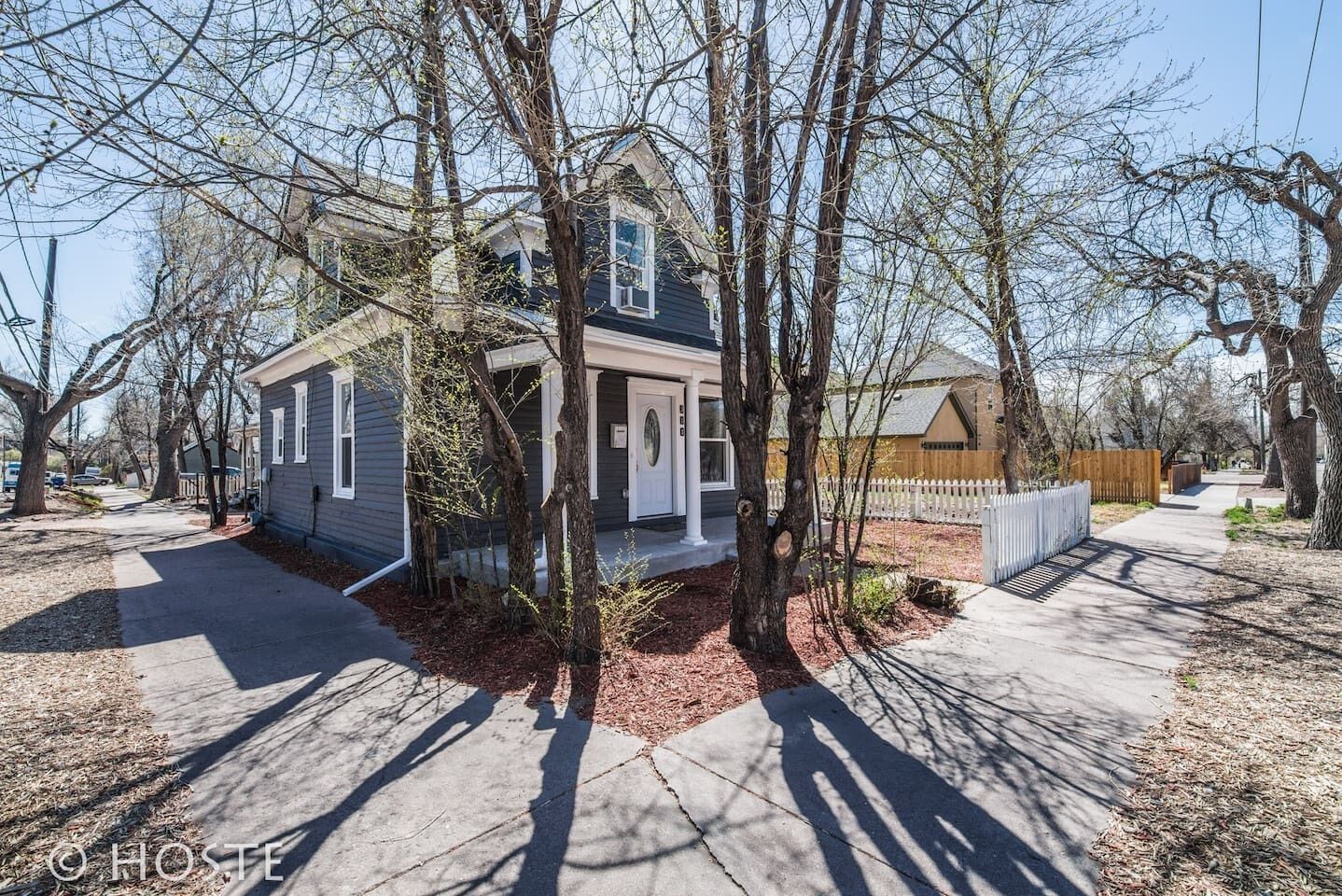 A two-story house with a front porch, surrounded by trees and a white picket fence.
