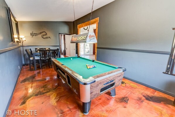 Een pooltafel in een ruimte met een eethoek, een wandklok en een bordje met 'Bud Light'.