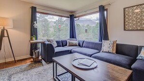 Un salon moderne avec un canapé d’angle, une table basse et une grande fenêtre agrémentée de rideaux.