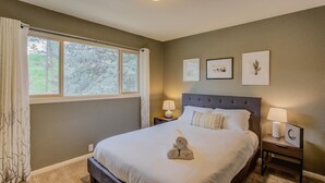 Une chambre à coucher avec un grand lit, deux tables de chevet, une fenêtre avec des rideaux et trois tableaux encadrés accrochés au mur.