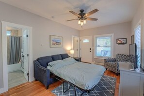 Une chambre à coucher avec un lit, un ventilateur de plafond, une fenêtre avec des stores, une chaise et un bureau.