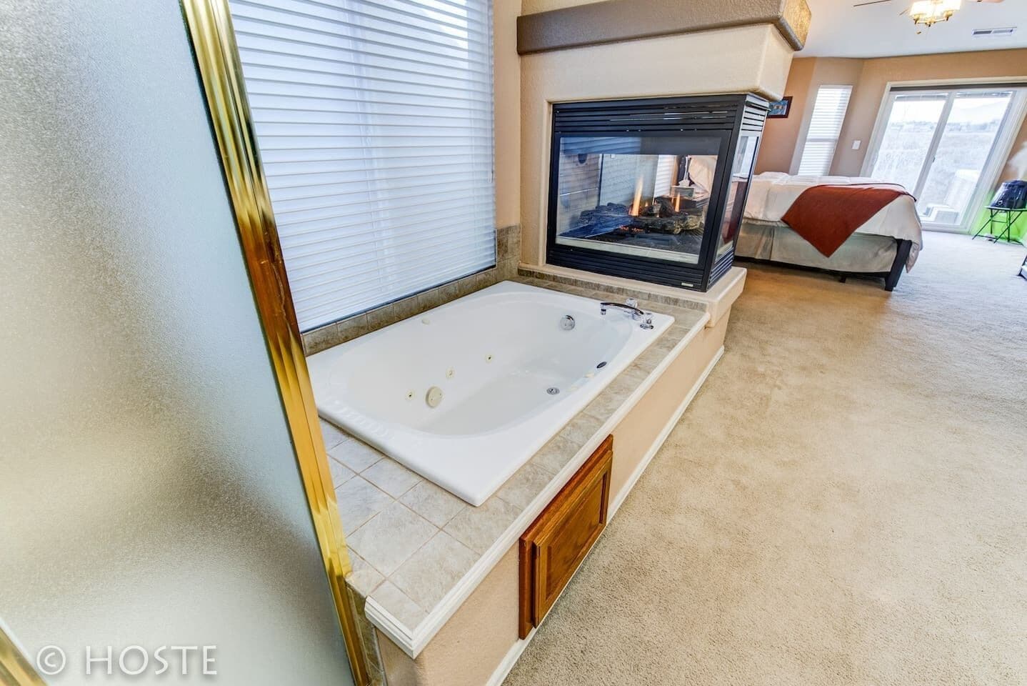 A modern bathroom with a large bathtub, a fireplace, and a bed in the background.