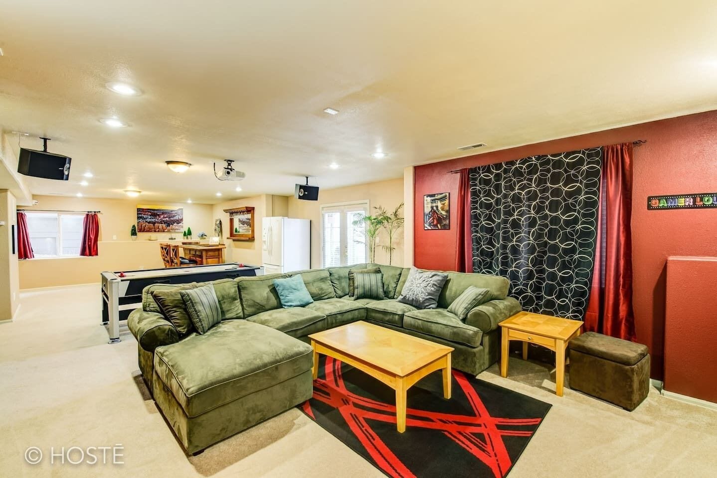 A living room with a green sectional sofa, a wooden coffee table, and a red and black rug.
