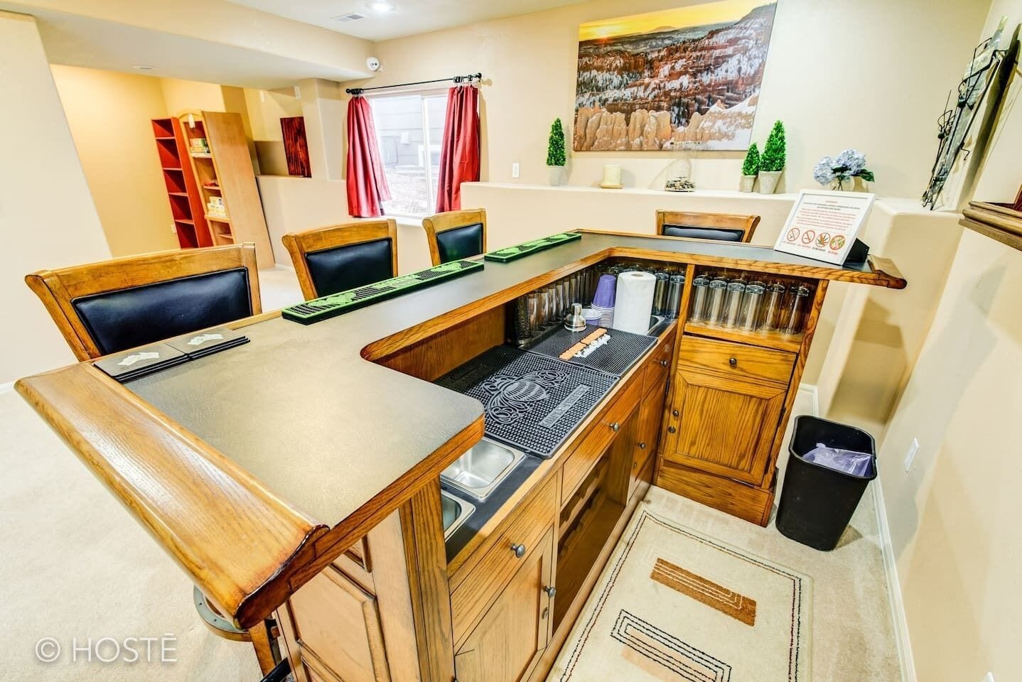Une cuisine compacte avec une table en bois, des chaises et un four encastré. On y trouve des placards, une poubelle et une fenêtre avec des rideaux.