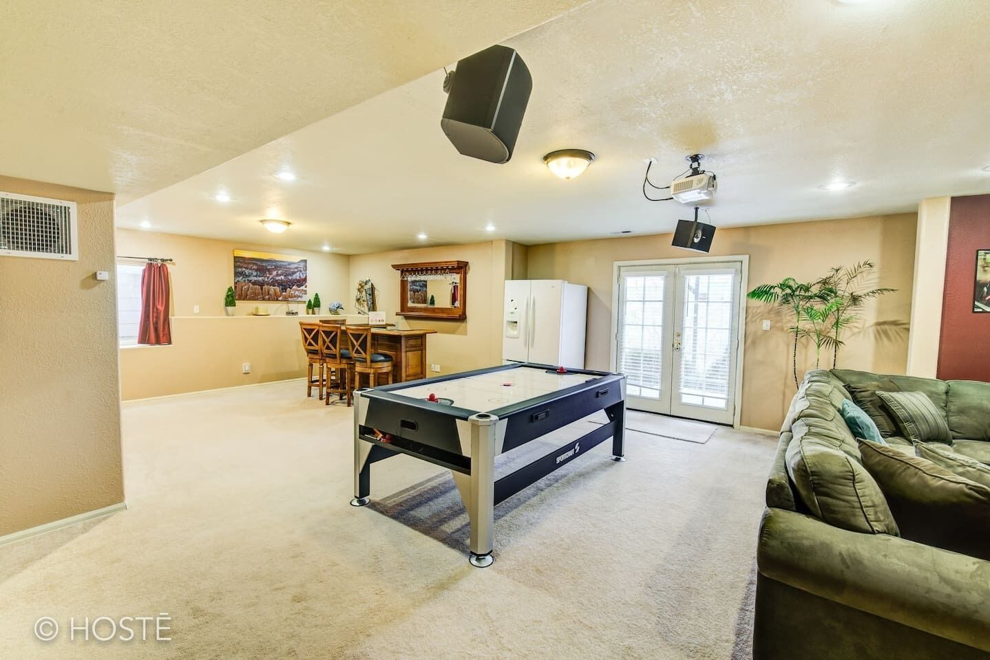 A spacious living area with a pool table, a dining table with chairs, a kitchen area, and a green couch.