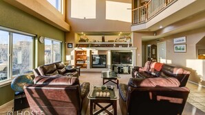 A spacious living room with leather sofas, a glass coffee table, and a fireplace. There is a balcony with a railing and a view of the outside. - 5BR Mtn Views Family Getaway HOT TUB (Colorado Springs)