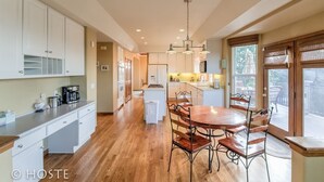 A spacious kitchen with white cabinets, a wooden dining table with chairs, and a large window providing natural light.