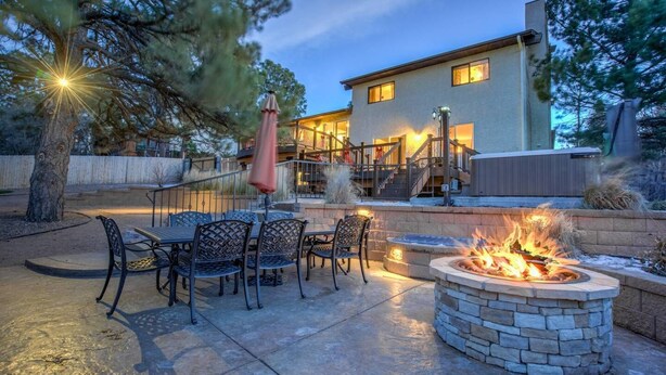 A patio with a stone fire pit and outdoor furniture, a covered seating area, and a house with a staircase leading to the upper level. - 4BR Entertainer AF Academy Hot Tub, Firepit! (Colorado Springs)