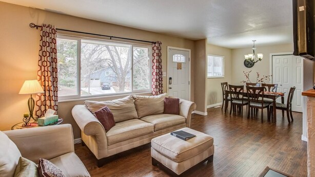 A living room with a beige sofa, a small ottoman, a dining table with chairs, and a kitchen area with a stove. - 4BR Dog Friendlygarden of the Godsbbq Grill! (Colorado Springs)