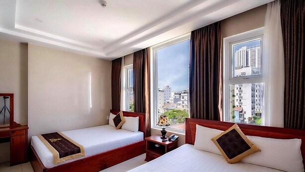 A hotel room with two beds, a desk, and a large window with a city view. - Dubai Hotel (Da Nang)