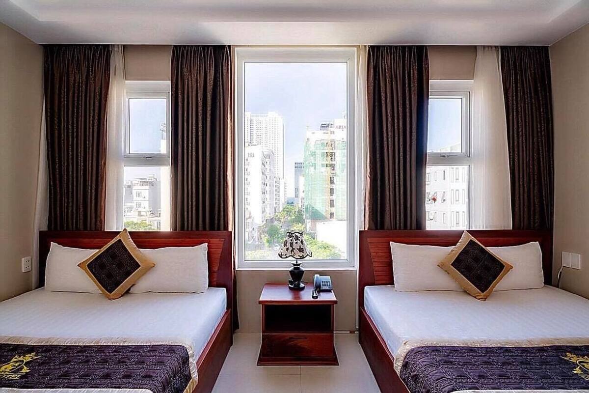 A hotel room with two beds, a nightstand, and a view of tall buildings.