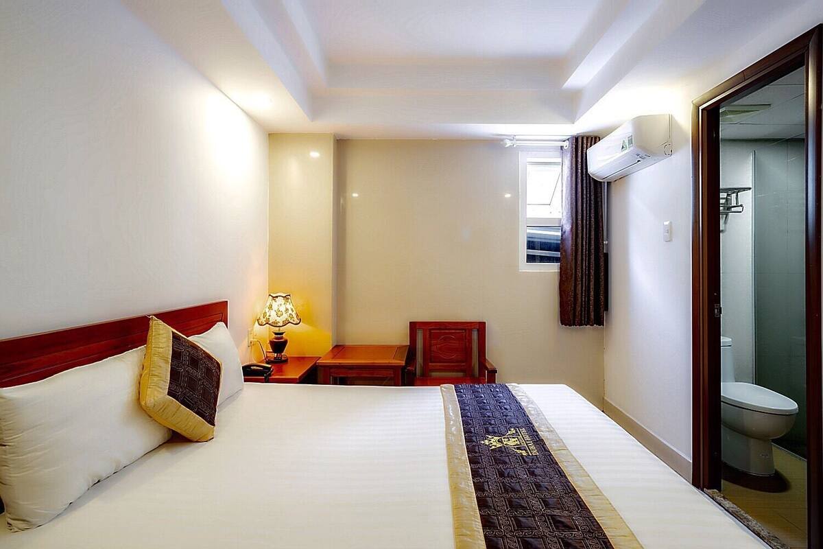 A hotel room with a bed, bedside table, lamp, and a view of the bathroom.