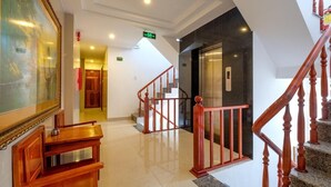 A lobby with a wooden desk, a framed painting, a staircase with red railings, and an elevator. - Dubai Hotel (Da Nang)